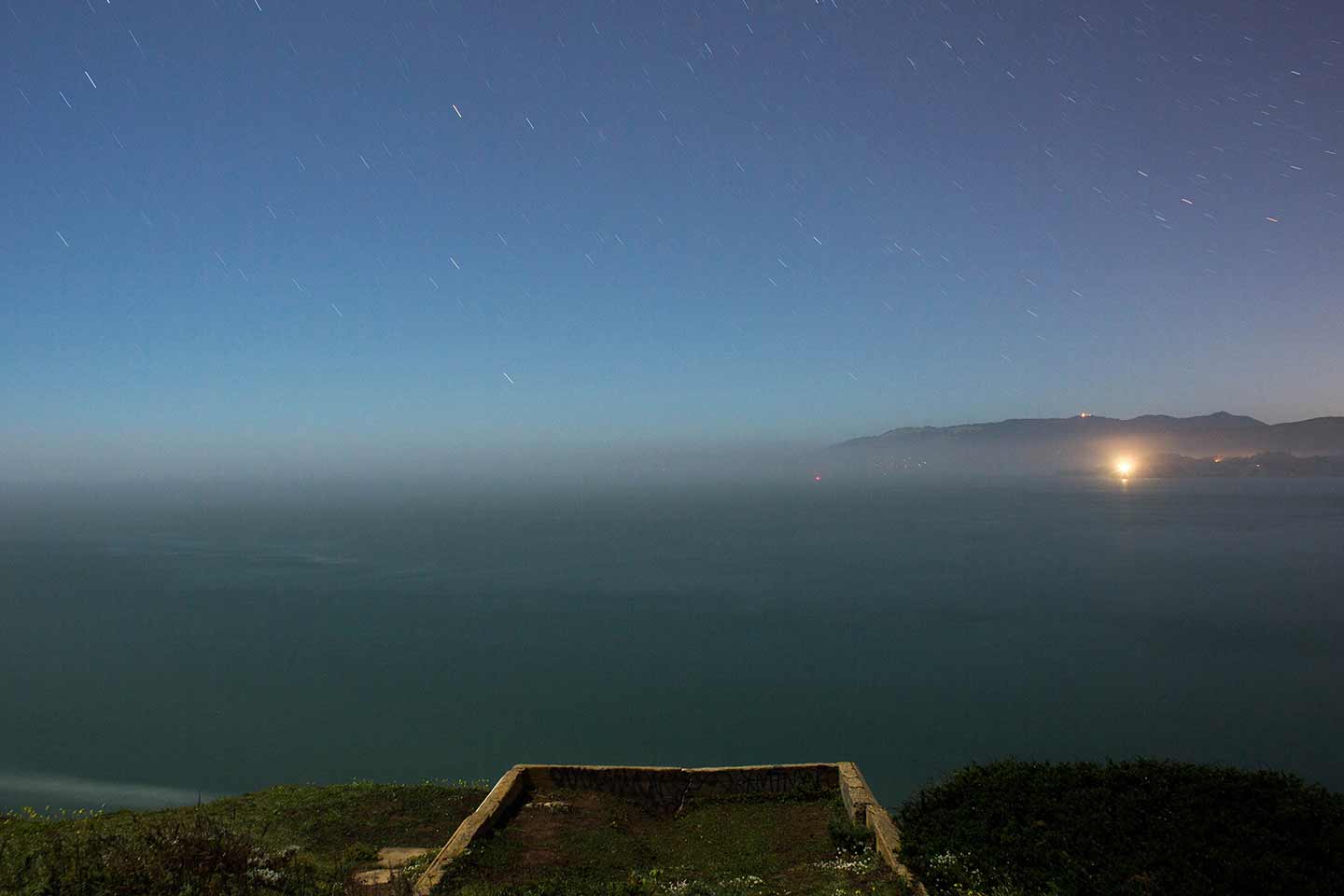 Photo of the foundations of a building on a cliff overlooking a lighthouse.